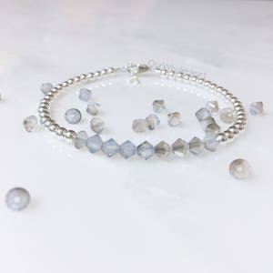 May include: A silver beaded bracelet with a row of clear iridescent glass beads. The bracelet is on a white surface with loose beads scattered around it. The text "OurWholeHeart" is visible in the image.