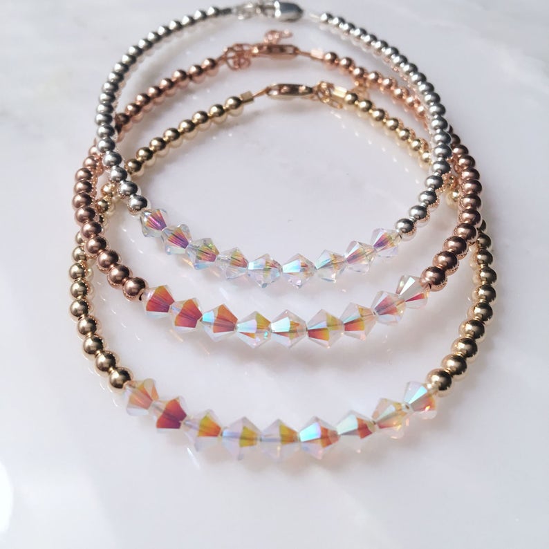 May include: Three delicate bracelets with iridescent crystal beads. The bracelets are layered in gold, rose gold, and silver.