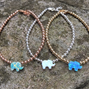 May include: Three silver beaded bracelets with opal elephant charms. The bracelets are in rose gold, silver, and gold.