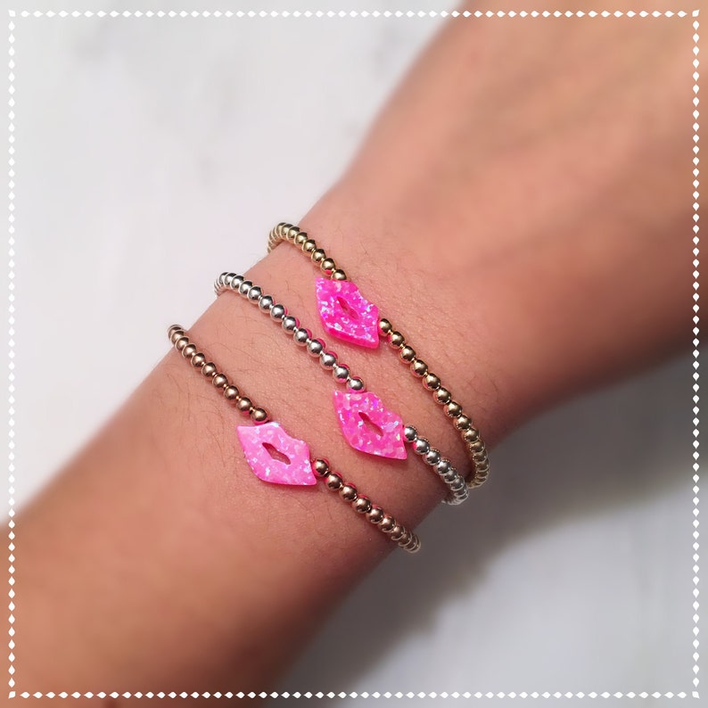 Puede incluir: Tres pulseras con dijes de labios rosas. Las pulseras est&aacute;n hechas de cuentas doradas, plateadas y de oro rosa.