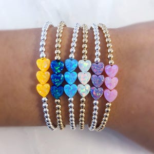 May include: Five bracelets with a silver and gold bead chain and three opal heart charms in different colors: yellow, blue, white, pink, and lavender.