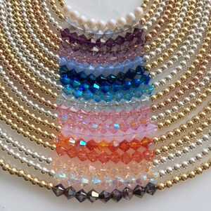 May include: A rainbow of crystal beads strung on gold, silver, and rose gold chains. The beads are arranged in a semi-circle, with the gold chain at the top and the silver chain at the bottom.