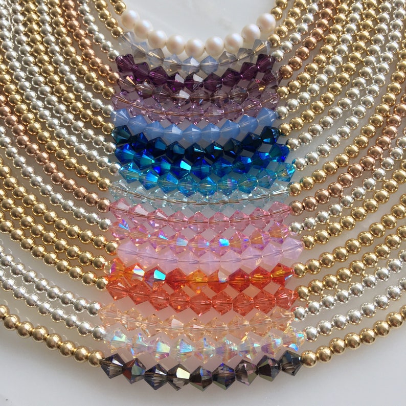 May include: A rainbow of crystal beads strung on gold, silver, and rose gold chains. The beads are arranged in a semi-circle, with the gold chain at the top and the silver chain at the bottom.