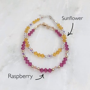 May include: Two beaded bracelets, one with yellow and clear beads labeled "Sunflower" and the other with pink and clear beads labeled "Raspberry".
