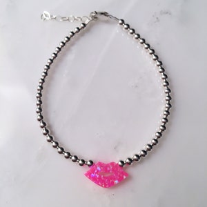 Puede incluir: Un brazalete de cuentas plateadas con un dije de labios de &oacute;palo rosa.