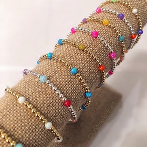 May include: A display of colorful beaded bracelets with gold and silver beads. The bracelets are stacked on a burlap-covered stand. The text "Our Whole Heart" is visible on the stand.