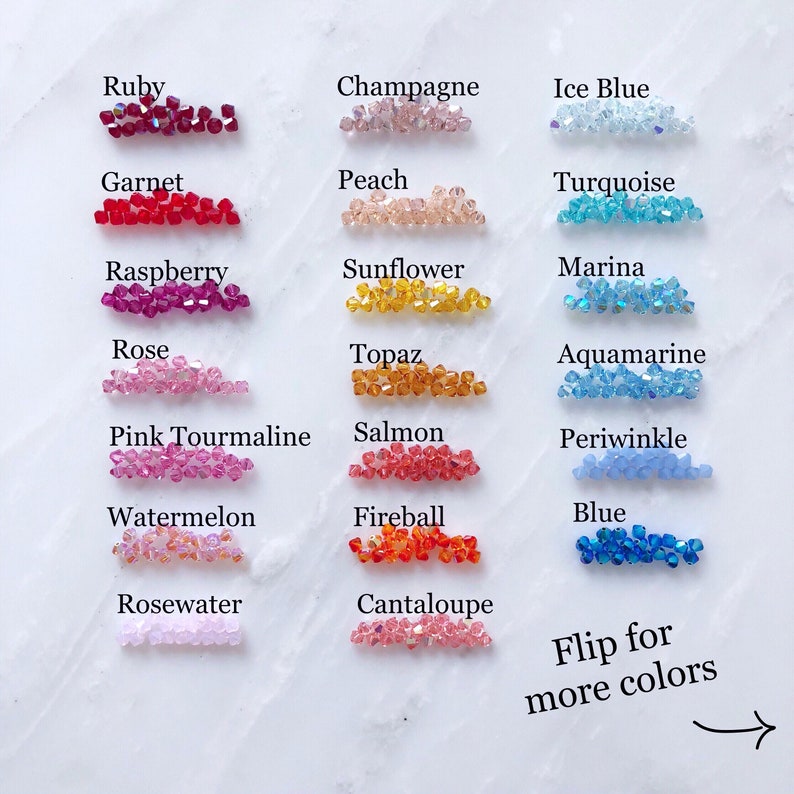 May include: A chart of 18 different colors of crystal beads, labeled with names like Ruby, Garnet, Raspberry, Rose, Pink Tourmaline, Watermelon, Rosewater, Champagne, Peach, Sunflower, Topaz, Salmon, Cantaloupe, Ice Blue, Turquoise, Marina, Aquamarine, Periwinkle, Fireball, and Blue. The text "Flip for more colors" is at the bottom of the chart with an arrow pointing to the right.