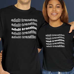 May include: Two people wearing black t-shirts with the text "adult transition" repeated on each shirt. The shirts are a dark black color and the text is in white.