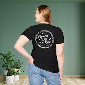 May include: Black t-shirt with a white circle graphic that says "Supporting my Elevator Operator for Life - Elevator Wife Club - Proud Member Since [Year]".