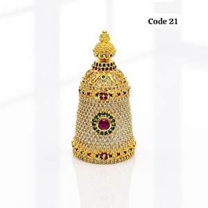May include: A gold-colored, jeweled bell-shaped ornament. The ornament is 2 inches high and 1 inch in diameter. It is adorned with clear, red, and green gemstones. The text "Code 21" is visible.