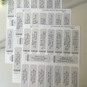 May include: A set of white rectangular stickers with black text. Each sticker features a different scripture reference from the Book of Mormon. The stickers are labeled with the book, chapter, and verses. The stickers are arranged in a grid pattern.