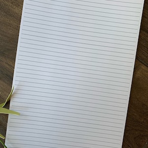 May include: A blank white sheet of paper with lined paper, ready for writing or drawing. The paper is on a wooden surface.
