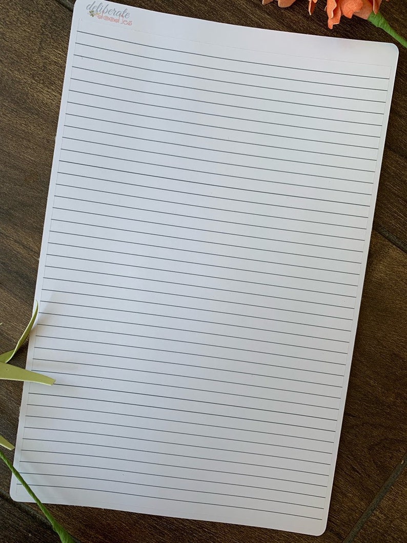 May include: A blank white sheet of paper with lined paper, ready for writing or drawing. The paper is on a wooden surface.