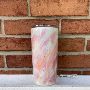 Puede incluir: Un vaso blanco con un dise&ntilde;o de remolino rosa y naranja y detalles de purpurina.