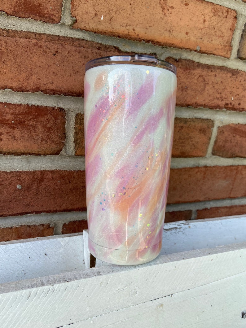 Puede incluir: Un vaso blanco con un dise&ntilde;o marmoleado rosa y naranja y detalles de purpurina.