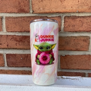 Puede incluir: Un vaso blanco con un dise&ntilde;o de remolino rosa y naranja. El vaso presenta una imagen de dibujos animados de un extraterrestre verde sosteniendo una rosquilla rosa. El texto "Dunkie Junkie" est&aacute; impreso en el vaso.