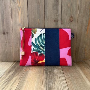 May include: A rectangular clutch with a gold zipper and a red tassel. The clutch features a patchwork design with floral and solid fabric panels in red, pink, white, and navy blue. A small tag is attached to the side.