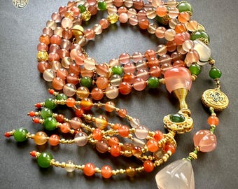 May include: A multi-strand necklace featuring a variety of beads in shades of orange, pink, green, and gold. The necklace includes a pendant with a teardrop-shaped stone and intricate gold detailing. The beads are strung on gold-colored wire.