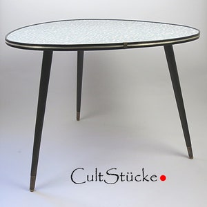 Könnte beinhalten: Ein dreieckiger Beistelltisch im Mid-Century-Modern-Stil mit gemusterter Tischplatte und dunklen Beinen. Der Tisch hat eine schwarze Umrandung mit goldenen Akzenten und messingfarbenen Füßen. Der Tisch ist ca. 61 cm breit und 51 cm hoch.