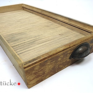 May include: A distressed wooden drawer with a metal handle. The drawer is made from light-coloured wood, showing the grain, and has a worn appearance. The text "CultStücke" is visible in the lower left corner.