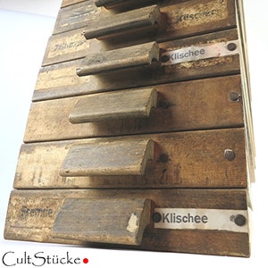 May include: A wooden drawer unit with multiple drawers, each with a wooden pull handle. The drawers are labeled with the word "Klischee".