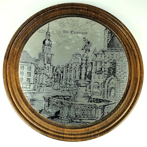 Peut inclure: Miroir rond encadré de bois, avec une image gravée détaillée d'une place de ville européenne, comprenant une fontaine et des bâtiments. La surface du miroir reflète la scène en niveaux de gris, avec le texte "Alt-Dortmund" en haut.