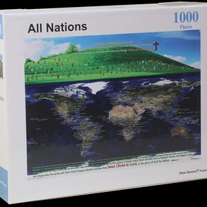 Op de afbeelding: Een witte doos met een puzzel van 1000 stukjes met de titel "All Nations". De puzzel toont een groene heuvel met figuren, een kruis en een wereldkaart. Tekst bevat "All Nations" en bijbelverzen.