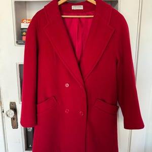 May include: A bright red double-breasted coat with a classic lapel collar and two front pockets. The coat is hanging on a wooden hanger. The brand name "FORECASTER" is visible on the label.