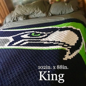 May include: A King-sized, navy blue, green, white, and gray crocheted blanket. The blanket features a large design of a stylized eagle. The blanket measures 102 inches by 88 inches.