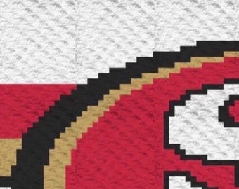 May include: A pixelated graphic design featuring a red circular emblem with a thick black and gold border. The emblem is set against a white background with a horizontal red stripe. The design displays a textured, grid-like pattern throughout.