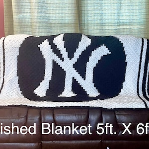 May include: A black and white crocheted blanket with the New York Yankees logo, draped over a brown leather couch. The blanket measures 5ft x 6ft.