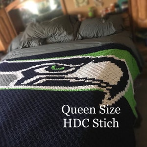 May include: A handmade, queen-size crochet blanket featuring the Seattle Seahawks logo. The blanket is primarily navy blue, with white, green, and gray accents. The text "Queen Size HDC Stich" is visible on the blanket.