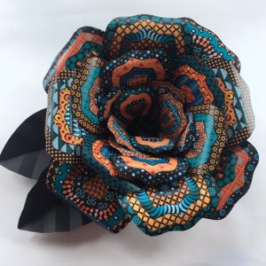 May include: A large paper flower with intricate patterns in shades of orange, blue, and black. The flower is made of multiple layers of paper, each with a different design. The flower is a decorative piece that can be used to add a touch of color and whimsy to any room.