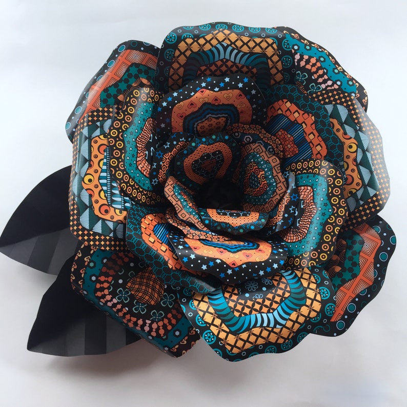 May include: A large paper flower with intricate patterns in shades of orange, blue, and black. The flower is made of multiple layers of paper, each with a different design. The flower is a decorative piece that can be used to add a touch of color and whimsy to any room.