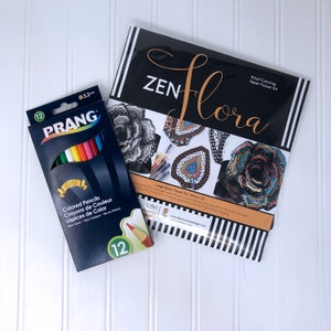 May include: A set of 12 colored pencils in a blue box with the brand name "PRANG" and the text "Colored Pencils, Crayons de Couleur, L&aacute;pices de Color". The box is next to a black and white paper flower kit with the text "ZEN flora Adult Coloring Paper Flower Kit" and "Large Paper Flower Kit Version 02".