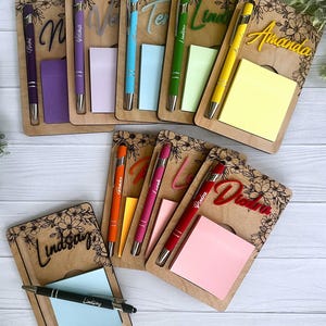 K&ouml;nnte beinhalten: Ein Set personalisierter Notizbl&ouml;cke aus Holz mit Stiften. Jeder Notizblock hat einen anderen Namen und ein Blumenmuster. Die Notizbl&ouml;cke sind in verschiedenen Farben, darunter Lila, Rosa, Gelb, Gr&uuml;n und Blau.
