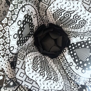 May include: Black and white paper flower with a geometric pattern. The flower is made of multiple layers of paper, each with a different pattern. The center of the flower is a black circle.