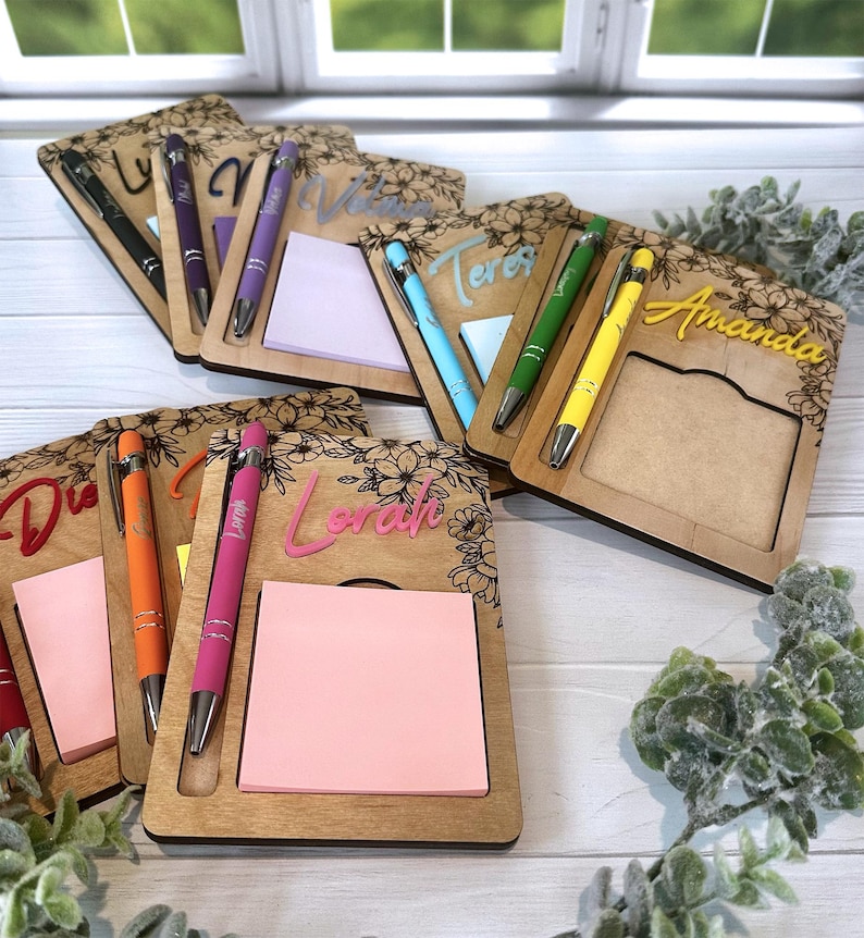 K&ouml;nnte beinhalten: Sechs Notizbl&ouml;cke aus Holz mit Blumendesigns und personalisierten Namen. Jeder Notizblock hat einen Haftnotizblock und einen Stift. Die Namen sind "Lora", "Vivian", "Teresa", "Amanda", "Diana" und "Lora".