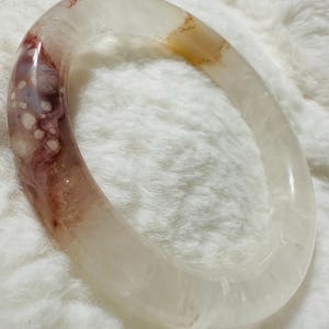 May include: A white agate bangle with brown and pink swirls and speckles.
