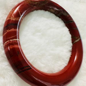 May include: A red, white, and brown banded bangle bracelet made of polished stone.