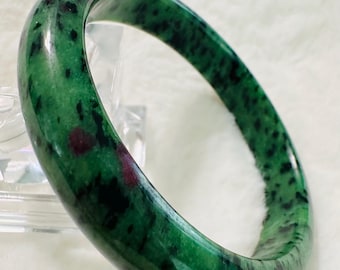 May include: A green jade bangle with dark green and red inclusions. The bangle is polished and has a smooth surface.