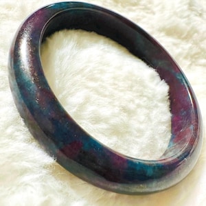 May include: A dark purple and teal jade bangle bracelet. The bangle is smooth and polished.