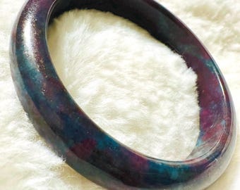 May include: A dark purple and teal jade bangle bracelet. The bangle is smooth and polished.