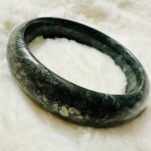 May include: A dark green bangle bracelet with silver flecks throughout. The bracelet is made of a smooth, polished material.