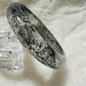 May include: A white bangle bracelet with black flecks throughout. The bracelet is made of a smooth, polished material.