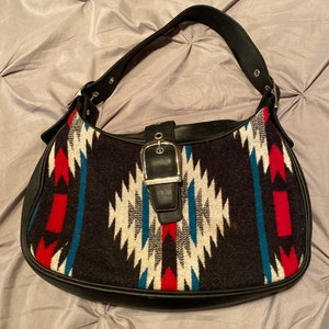 May include: Black leather shoulder bag with a geometric patterned fabric flap. The flap features red, white, and blue colors.