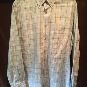 May include: A light blue long-sleeved button-down shirt with a white and black plaid pattern. The shirt has a pocket on the left side and the words "Wrinkle Resistant" on the tag.