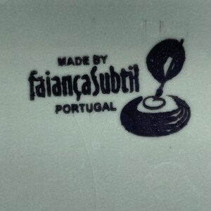 K&ouml;nnte beinhalten: Nahaufnahme einer hellgr&uuml;nen Keramikoberfl&auml;che mit den Worten "MADE BY faian&ccedil;asubtil PORTUGAL" in Schwarz. Eine schwarze Grafik eines stilisierten Designs ist ebenfalls vorhanden.