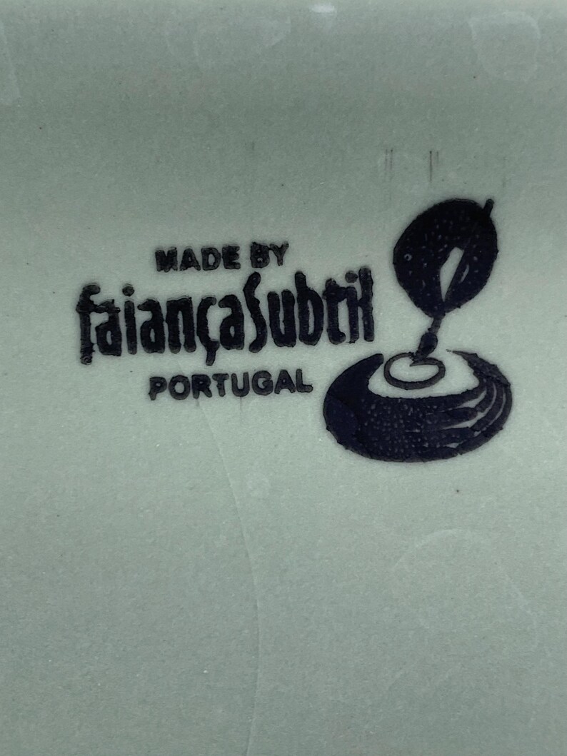 K&ouml;nnte beinhalten: Nahaufnahme einer hellgr&uuml;nen Keramikoberfl&auml;che mit den Worten "MADE BY faian&ccedil;asubtil PORTUGAL" in Schwarz. Eine schwarze Grafik eines stilisierten Designs ist ebenfalls vorhanden.