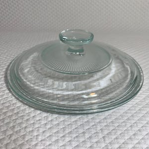 May include: A clear glass lid with a round knob. The lid has a ridged design on the inside and is likely for a pot or pan. The lid is made of clear glass.